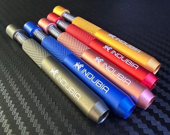 May include: Five cylindrical metal tools with knurled grips and threaded ends, arranged diagonally. Each tool features the brand name INDUBIA and a lion logo printed in white. The colors are olive green, blue, copper, red, and gold, all metallic.