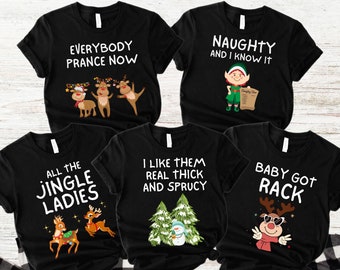 May include: Black t-shirts with Christmas-themed graphics and text. Designs include reindeer, elves, and phrases like "Everybody Prance Now" and "Naughty and I Know It." The shirts are displayed on a plaid background.