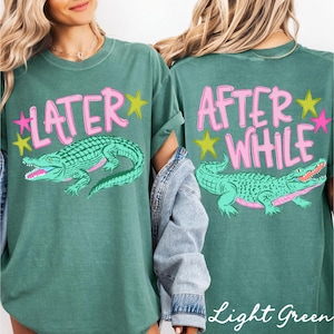 May include: Light green t-shirt with a front graphic of a green alligator and the word "LATER" in pink. The back of the shirt features the words "AFTER WHILE" and a matching alligator graphic. Pink and yellow star accents complete the design.