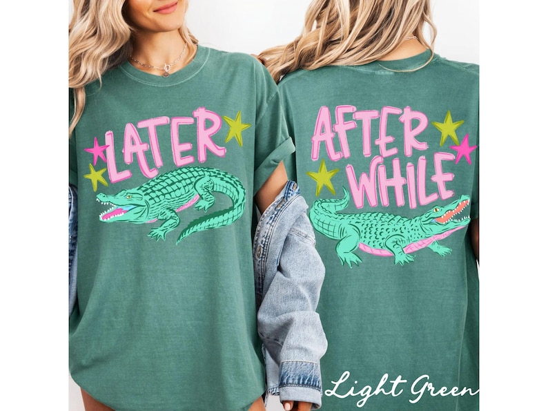 May include: Light green t-shirt with a front graphic of a green alligator and the word "LATER" in pink. The back of the shirt features the words "AFTER WHILE" and a matching alligator graphic. Pink and yellow star accents complete the design.
