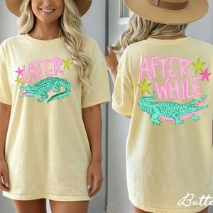 May include: Butter yellow t-shirt with a front graphic of a teal alligator and the word "LATER" in pink. The back of the shirt features the words "AFTER WHILE" and a matching alligator design. The shirt has a relaxed fit.