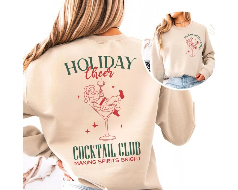 K&ouml;nnte beinhalten: Beiges Sweatshirt mit festlichem Design. Auf der R&uuml;ckseite befindet sich eine Illustration des Weihnachtsmanns in einem Martini-Glas mit den Worten "HOLIDAY CHEER" und "COCKTAIL CLUB". Auf der Vorderseite befindet sich eine kleinere Version des Designs und die Worte "FULL OF HOLIDAY SPIRIT".