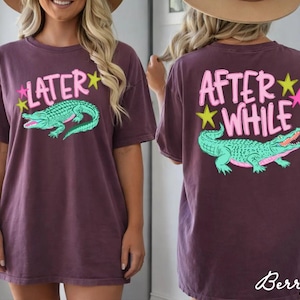May include: Berry-colored t-shirt with a front graphic that says "Later" above a green alligator. The back of the shirt says "After While" above a matching alligator. Pink and yellow stars accent the text.