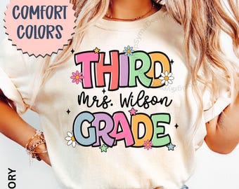 May include: Ivory-colored t-shirt with the words "THIRD Mrs. Wilson GRADE" in colorful, retro-style lettering. The design includes flower and star accents. The words "COMFORT COLORS" are in a pink circle in the upper left corner.