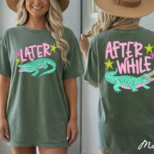 May include: Olive green t-shirt with a front graphic that says "LATER" above a teal alligator illustration. The back of the shirt says "AFTER WHILE" above a matching alligator graphic. Pink and yellow star accents are included.