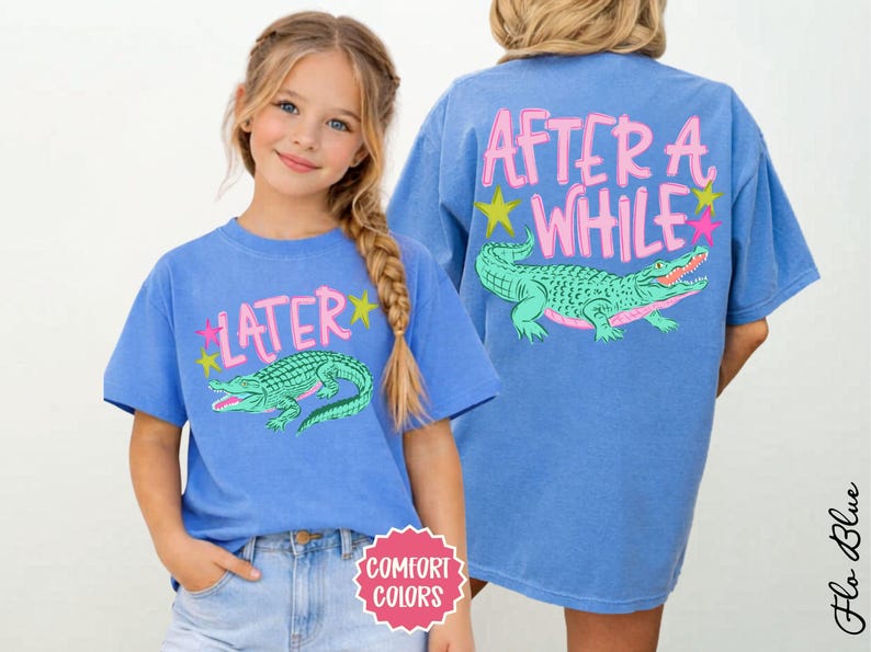May include: Blue t-shirts with a cartoon alligator design. One shirt has "LATER" and the other has "AFTER A WHILE" in pink text. Both shirts have a green alligator with pink accents and star graphics.