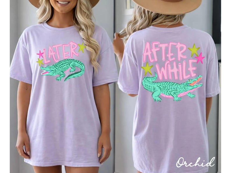 May include: A light purple t-shirt with a front and back design. The front features the word "LATER" above a green alligator graphic. The back says "AFTER WHILE" above a matching alligator. Both designs include star accents.