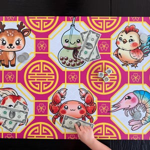 Puede incluir: Un tablero de juego colorido con animales y símbolos de dibujos animados. El tablero tiene un fondo rosa con patrones geométricos amarillos. Las ilustraciones incluyen un ciervo, una bebida boba, un pollo, un pez, un cangrejo y un camarón. Billetes de dólar estadounidense y monedas están colocados en el tablero.