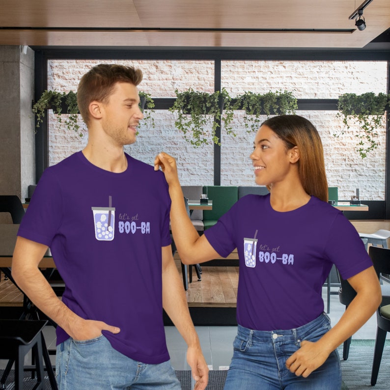 May include: Two people wearing matching purple t-shirts. Each shirt features a graphic of a bubble tea with the text "let's get BOO-BA" in light purple. The bubble tea graphic includes a straw and boba pearls.