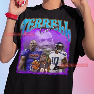 May include: Black t-shirt featuring a purple and blue graphic print of Terrell Owens, a renowned American football player. The graphic includes images of Owens in various uniforms, including the Philadelphia Eagles, Baltimore Ravens, and Cincinnati Bengals.