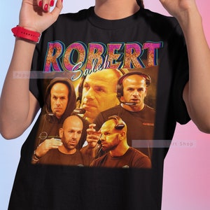 May include: Black t-shirt featuring a graphic print of four men's faces. The text "ROBERT Saleh" is printed in pink and blue glitter letters on the shirt.