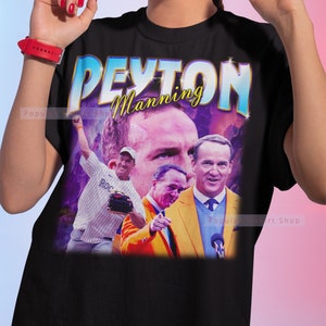 May include: Black t-shirt with a retro-style graphic of Peyton Manning. The graphic features a collage of images of Manning in different poses, including him throwing a football and speaking at a podium. The text "Peyton Manning" is written in a bold, colorful font.