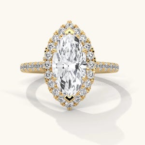 May include: A yellow gold ring featuring a large marquise-cut center stone surrounded by a halo of small round brilliant-cut stones. The band is also set with a row of small round stones along the top half of the shank.