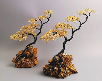 May include: Two wire bonsai trees with black trunks and golden wire foliage. The trees are mounted on textured, golden-brown rock bases. The bonsai trees are a decorative item.