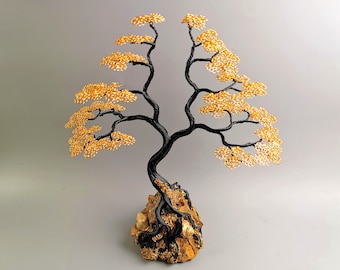 May include: A handcrafted wire tree sculpture with a black trunk and branches, and golden-yellow leaves. The tree is mounted on a textured, tan-colored base. The sculpture is a decorative art piece.
