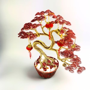 May include: A gold wire bonsai tree with red wire leaves and red lanterns hanging from the branches. The tree is in a red pot with white stones and red wire coins.