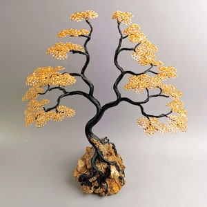May include: A handcrafted wire tree sculpture with a black trunk and branches, and golden yellow leaves. The tree is mounted on a natural rock base. This decorative piece is a unique home decor item.