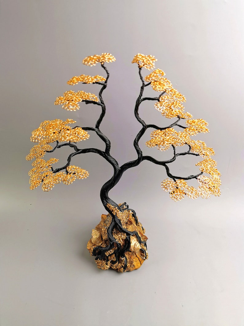 May include: A handcrafted wire tree sculpture with a black trunk and branches, and golden yellow leaves. The tree is mounted on a natural rock base. This decorative piece is a unique home decor item.
