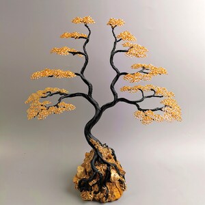 May include: A handcrafted wire tree sculpture with a black trunk and branches, and golden-colored leaves. The tree is mounted on a natural rock base. The sculpture is a decorative item.
