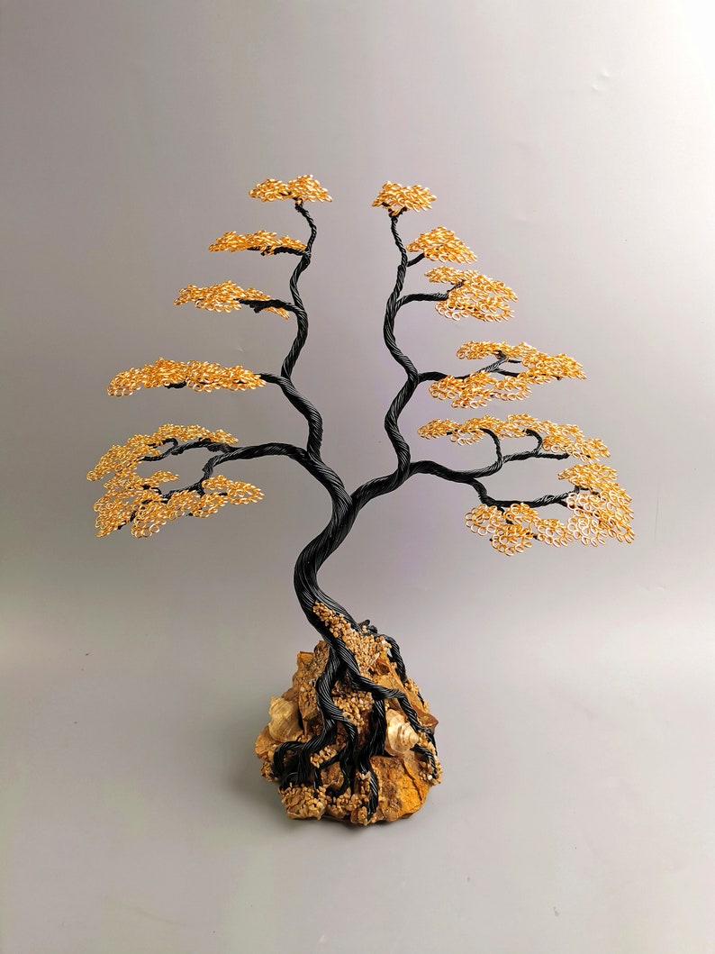May include: A handcrafted wire tree sculpture with a black trunk and branches, and golden-colored leaves. The tree is mounted on a natural rock base. The sculpture is a decorative item.