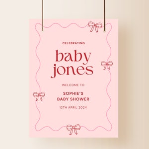 K&ouml;nnte beinhalten: Ein rosa Babyparty-Schild mit den Worten "baby jones" in fetter roter Schrift. Das Schild enth&auml;lt den Text "Celebrating", "Welcome to Sophie's Baby Shower" und das Datum "12th April 2024". Das Schild ist mit Schleifenillustrationen verziert.