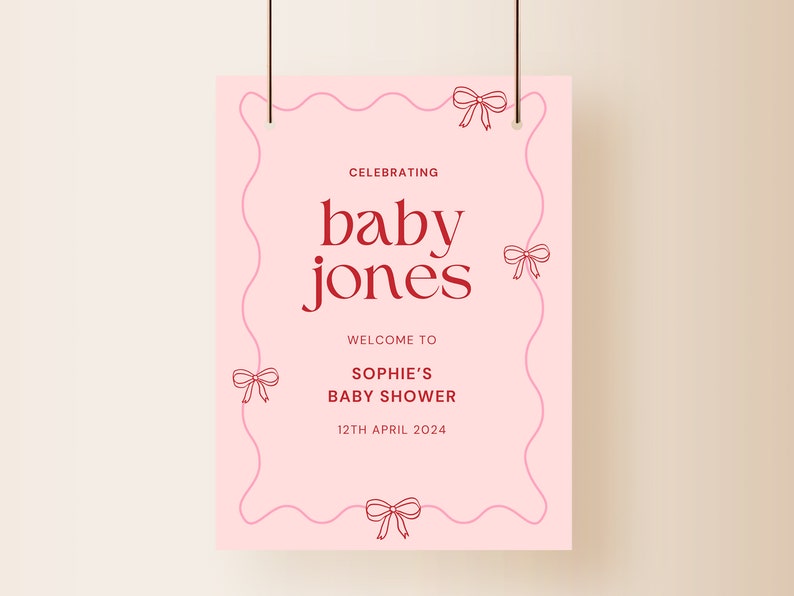 K&ouml;nnte beinhalten: Ein rosa Babyparty-Schild mit den Worten "baby jones" in fetter roter Schrift. Das Schild enth&auml;lt den Text "Celebrating", "Welcome to Sophie's Baby Shower" und das Datum "12th April 2024". Das Schild ist mit Schleifenillustrationen verziert.