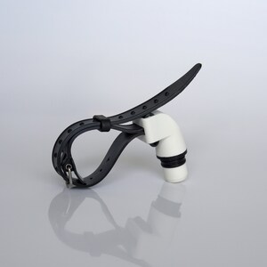 May include: A black adjustable strap with a white plastic spout. The strap is designed to hold a bottle or other object.