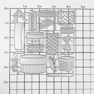 May include: A set of 12 metal die-cut shapes for crafting. The shapes include boxes, jars, bows, and other decorative elements. The shapes are approximately 5 inches wide and 5 inches tall.