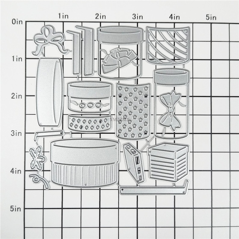 May include: A set of 12 metal die-cut shapes for crafting. The shapes include boxes, jars, bows, and other decorative elements. The shapes are approximately 5 inches wide and 5 inches tall.