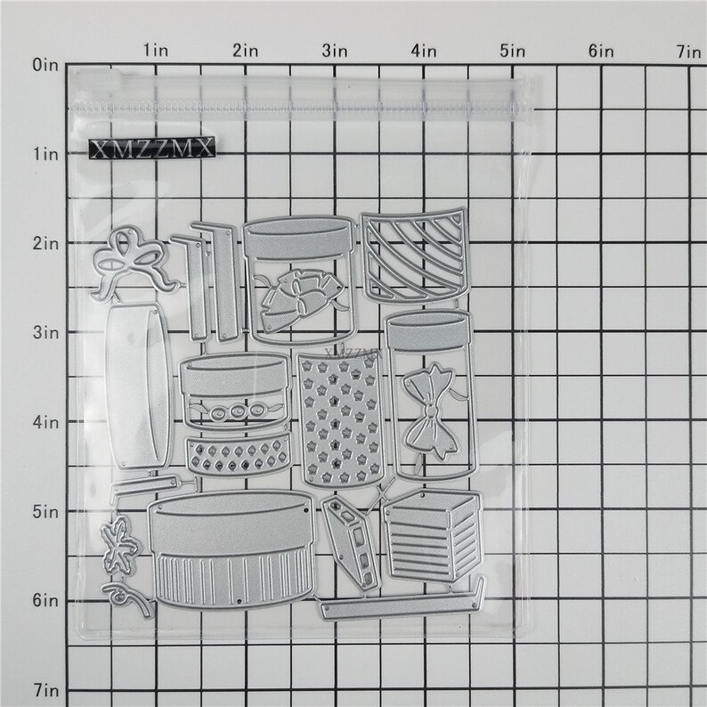 May include: A set of 14 metal die-cut shapes for crafting, including jars, boxes, bows, and stars. The shapes are in a clear plastic bag with a white grid background.