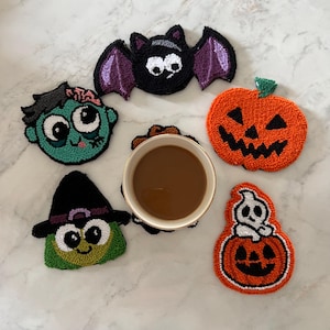 Może przedstawiać: Zestaw podkładek pod napoje o tematyce Halloween. Podkładki przedstawiają wzory nietoperza, dyni, ducha, zombie i czarownicy. Podkładki wykonane są z teksturowanego materiału i mają różne kolory.
