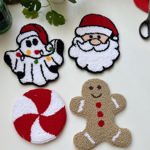 May include: Four handmade Christmas-themed felt ornaments: a candy cane, a gingerbread man, Santa Claus, and a ghost. The ornaments are all white with red and brown accents.