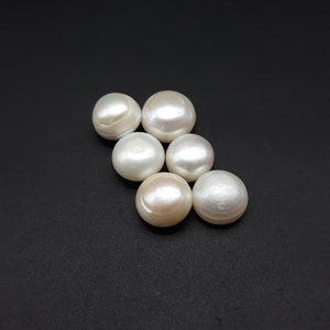Puede incluir: Seis perlas redondas y brillantes, de color blanco cremoso y brillo iridiscente, dispuestas sobre un fondo oscuro. Las perlas varían ligeramente de tamaño y tienen una superficie lisa y pulida que refleja la luz.