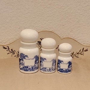 Peut inclure: Trois pots à épices en céramique blanche avec des motifs floraux bleus et blancs. Les pots ont des couvercles ronds et sont disposés en rangée du plus grand au plus petit.