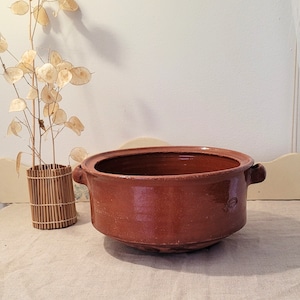 Puede incluir: Una olla grande, redonda, de terracota con dos asas. La olla es marrón y tiene una superficie rugosa y texturizada.