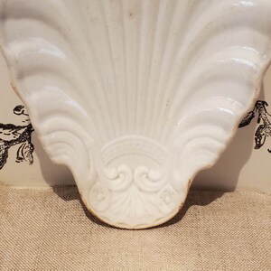 Puede incluir: Plato de cer&aacute;mica blanca en forma de concha con un dise&ntilde;o decorativo en la parte inferior.