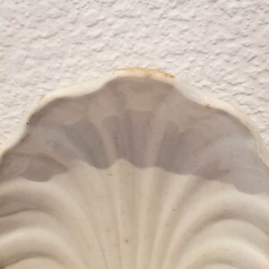 Puede incluir: Plato de cer&aacute;mica blanca en forma de concha de mar con un acabado liso y brillante.