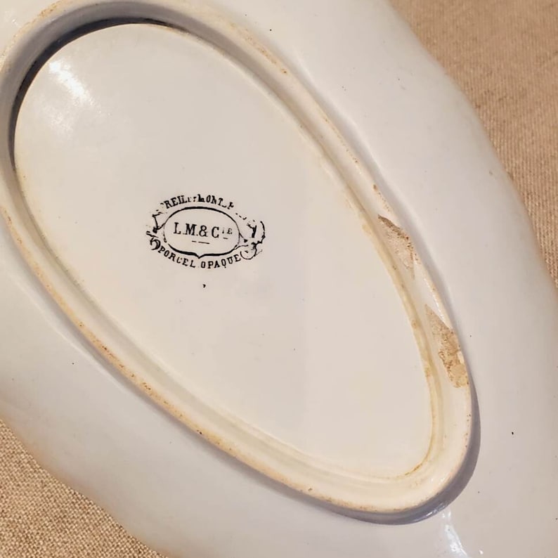 Puede incluir: Plato de servir ovalado de cer&aacute;mica blanca con una marca impresa en blanco y negro en la parte inferior que dice "REIL MONTRE L.M.&C.ie PORCEL OPAQUE".