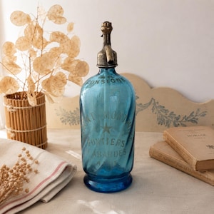 May include: A vintage blue glass bottle with a metal spout and the text "MONT FONTIERS ABARDES" in silver lettering. The bottle has a capacity of 105 cl. The bottle is a decorative item.