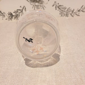 K&ouml;nnte beinhalten: Eine klare Glas Tasse mit einem wei&szlig;en und rosa Blumenmuster. Die Tasse ist umgedreht, wodurch der Boden der Tasse mit einem kleinen schwarzen Symbol sichtbar wird.