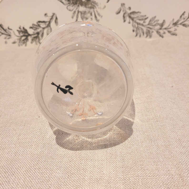 K&ouml;nnte beinhalten: Eine klare Glas Tasse mit einem wei&szlig;en und rosa Blumenmuster. Die Tasse ist umgedreht, wodurch der Boden der Tasse mit einem kleinen schwarzen Symbol sichtbar wird.