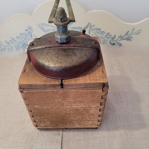 May include: An antique coffee grinder with a red and silver metal top and a wooden box base. The grinder has a crank handle and a small knob on top. The wood box is constructed with dovetail joints.