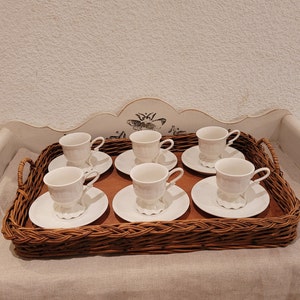 Peut inclure: Un ensemble de six tasses à thé et soucoupes en porcelaine blanche disposées sur un plateau en osier brun. Les tasses et les soucoupes ont un motif floral délicat.