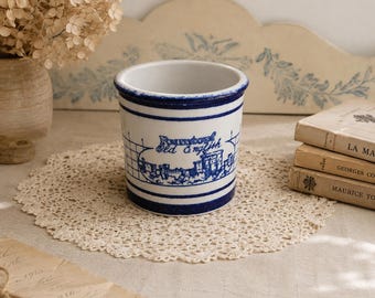 Peut inclure: Un pot en céramique blanc et bleu avec le texte "Bournemouth Old English" et une illustration de château. Le pot a un bord bleu et deux rayures bleues. Il repose sur un napperon en dentelle.