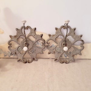 Peut inclure: Deux crochets muraux décoratifs avec un motif floral. Les crochets sont en métal et ont une finition blanche vieillie. Chaque crochet a un bouton en céramique blanche.