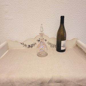 K&ouml;nnte beinhalten: Eine klare Glasflasche mit floralem Muster und einem Stopfen. Die Flasche steht auf einer wei&szlig;en Oberfl&auml;che mit floralem Muster. Eine Weinflasche steht ebenfalls auf der Oberfl&auml;che.