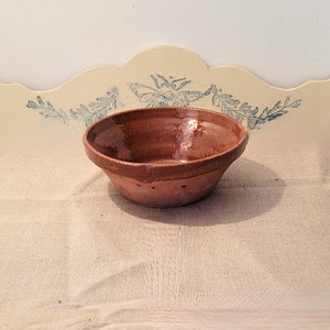 May include: A brown terracotta bowl with a glazed interior. The bowl has a slightly rounded shape and a wide rim.