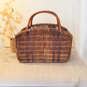 Peut inclure: Un panier en osier brun avec des rayures bleues et orange. Le panier a une poignée et est fait d'osier tressé.