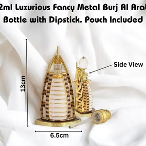 Puede incluir: Una r&eacute;plica de metal dorado del edificio Burj Al Arab en Dubai, un frasco de perfume de 12 ml con un aplicador. El frasco mide 13 cm de alto y 6,5 cm de ancho. El frasco est&aacute; sobre una superficie blanca.