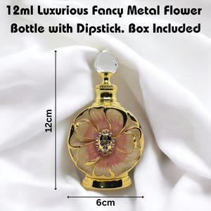 Puede incluir: Una botella de metal dorado con un dise&ntilde;o de flor rosa y blanca. La botella mide 12 cm de alto y 6 cm de ancho. Tiene un tap&oacute;n de vidrio transparente y viene con una caja.